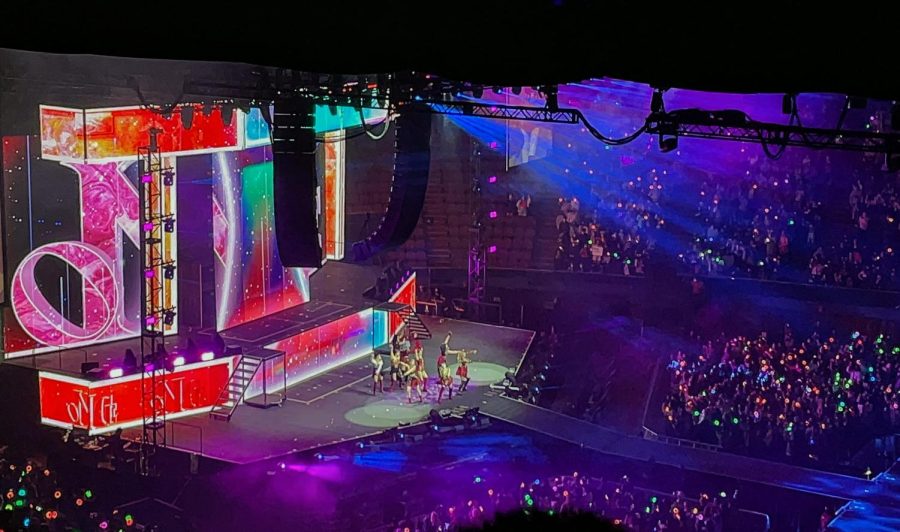 Stage lights shine on TWICE, illuminated by colorful lights held by members of the audience.