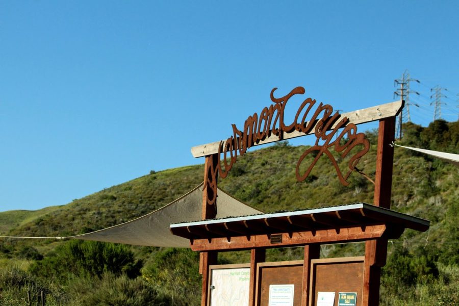 A trailhead welcomes all hikers to Harmon Canyon, nestled among green flowering hills.