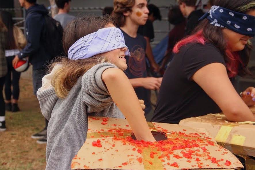 Students at the Fear Factor booth blindly reach into red jello in search of small objects.