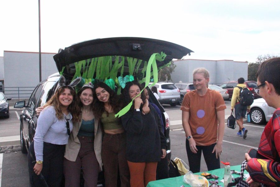 In front of their swamp-themed trunk, seniors Linda Manzo ‘23, Madison Thompson ‘23, Jasmine Guzman ‘23 and Kelsy Randall ‘23 show off their Shrek-inspired costumes while handing out waffles and candy to students who are dressed up for Halloween. 