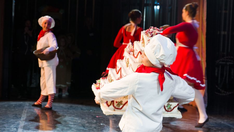 Finley Colavito ’26, adorned in a chef’s hat and coat, carries a large cake onto the stage while rehearsing the cook’s dance from the second act of The Nutcracker.