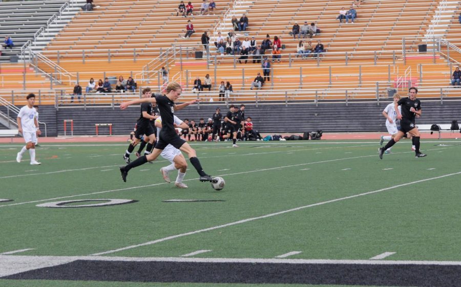 Connor Bursek ‘25 steals the ball from his opponent in an attempt to help take back control of the game. Cate chases close behind, as fans in the stands and players on the bench watch with anticipation.