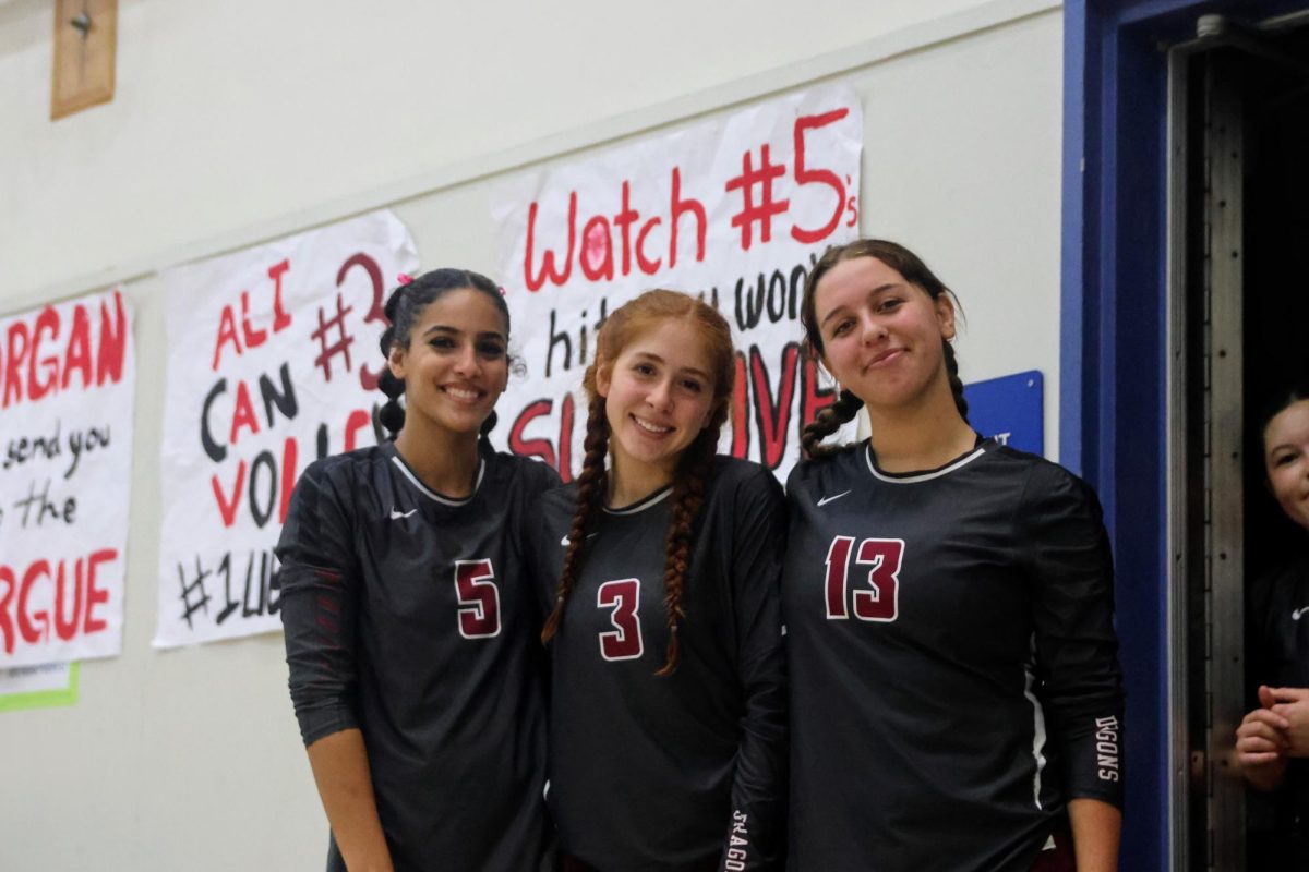 On the chilly night of Oct. 1, 2024, Foothill Technology High School (Foothill Tech) competes in a rivalry game against St. Bonaventure (Bonnie) for the second time this season. Mia Farag '25, Aliana Hantgin '25 and Fiona Aulenta '26 pose for the camera in between sets. Behind them are homemade posters, decorated with red and black, showing Dragon pride. These posters commemorate the four seniors on the team, making their last year special.