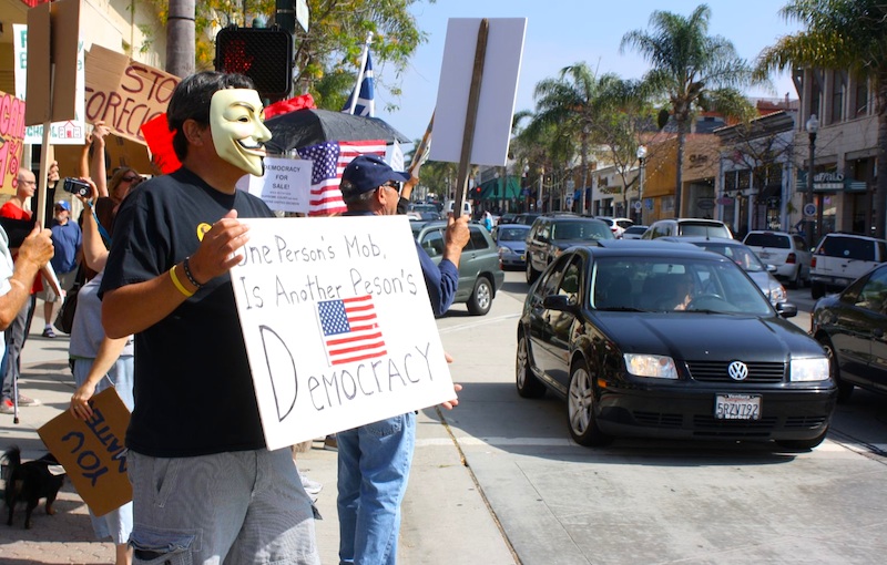 Standing outside of Bank of America, protesters held signs to spread their concern that the government represents corporate interests instead of the people. Credit: Aysen Tan/The Foothill Dragon Press.